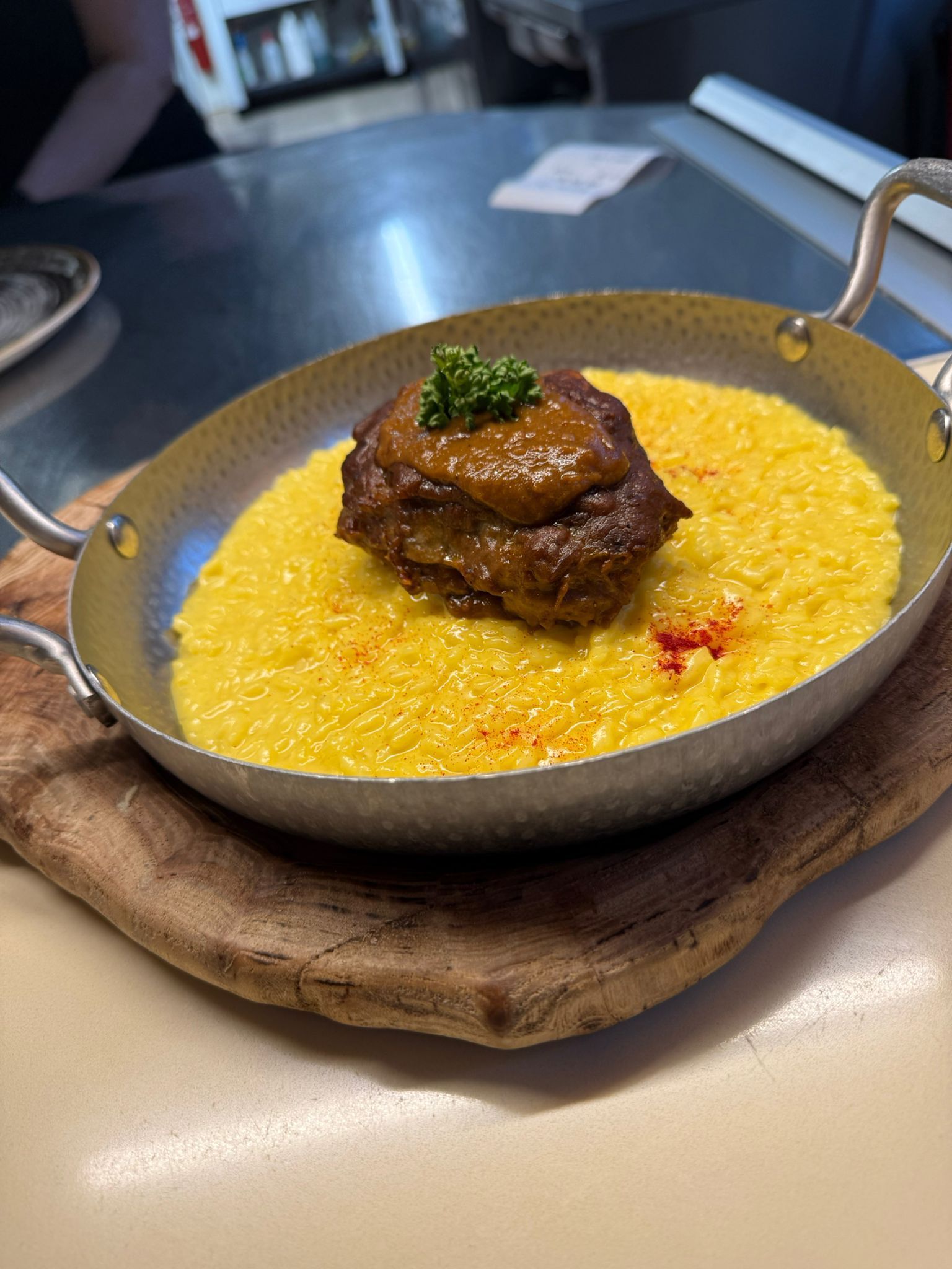Piatto in padella con polenta gialla cremosa, sormontato da un medaglione di carne brasata e prezzemolo su un tavolo