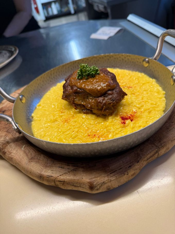Bistecca scottata in padella su polenta gialla cremosa in una padella grigia poco profonda su un tagliere di legno.