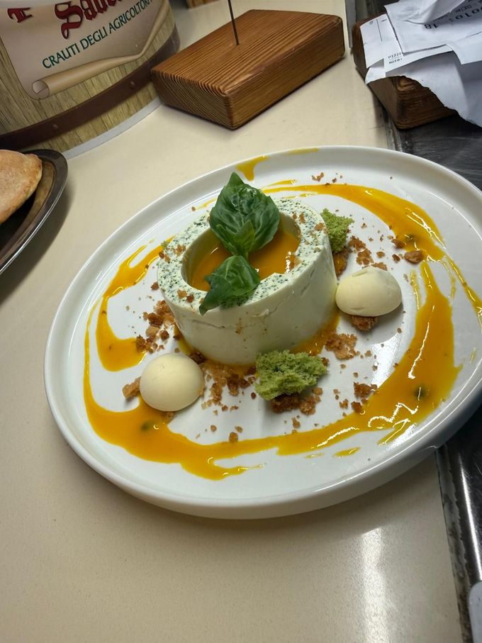 Dessert impiattato con salsa all'arancia, guarnizione di menta e palline di gelato bianco su un tavolo.