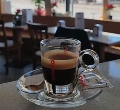 In un bar, una tazzina di caffè espresso su un piattino, con una bustina di zucchero accanto.