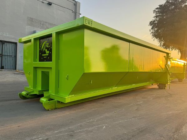 Bright neon-green industrial dumpster or container parked on a paved lot beside a building at sunset