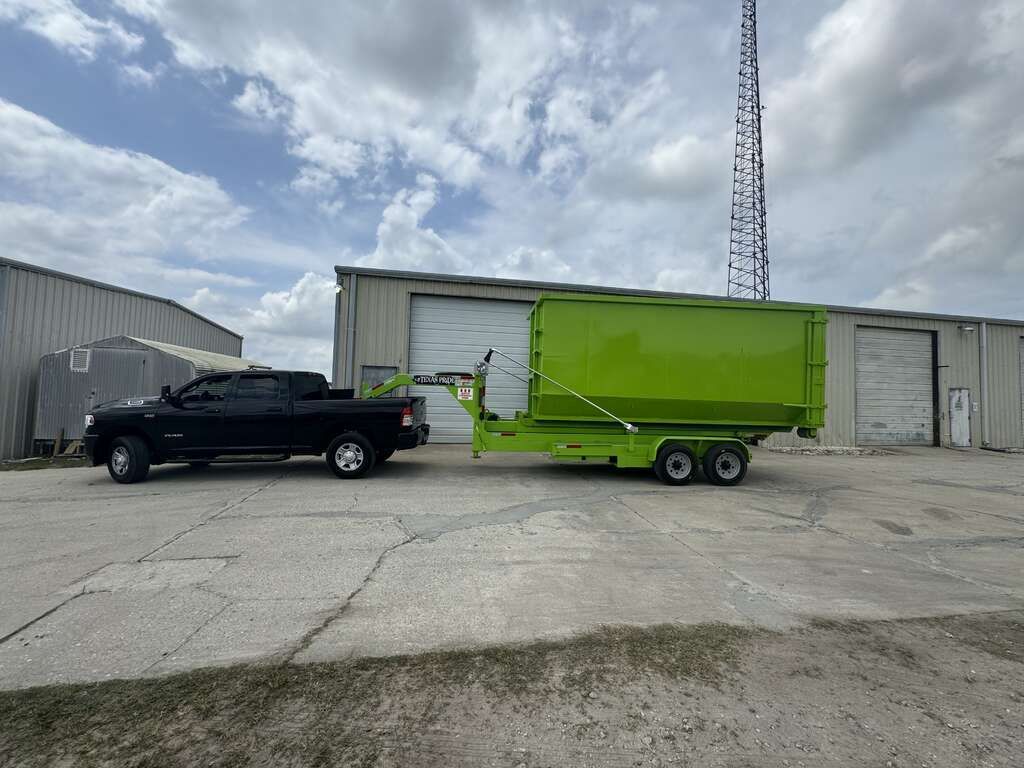 Black pickup truck towing a bright green trailer beside warehouse buildings under a cloudy sky