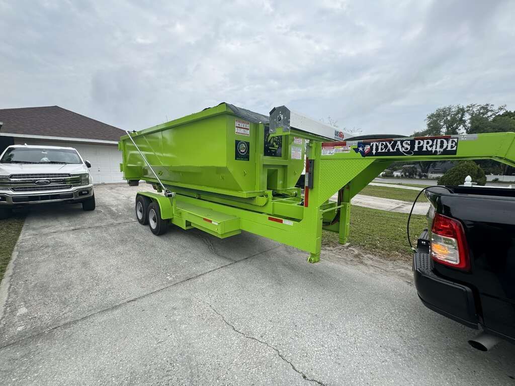 Bright green enclosed trailer parked on pavement beside vehicles, with a rear ramp and 