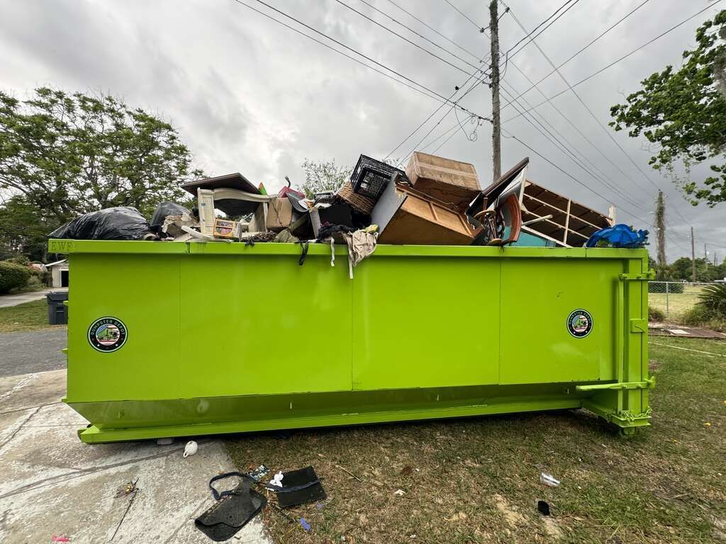 Bright green dumpster overflowing with furniture and trash on a roadside under power lines