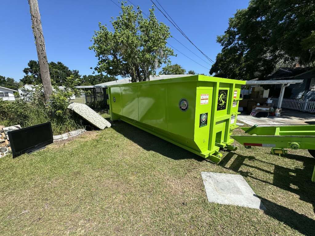 Bright green utility trailer tipped on its side in a grassy yard near a house and trees.