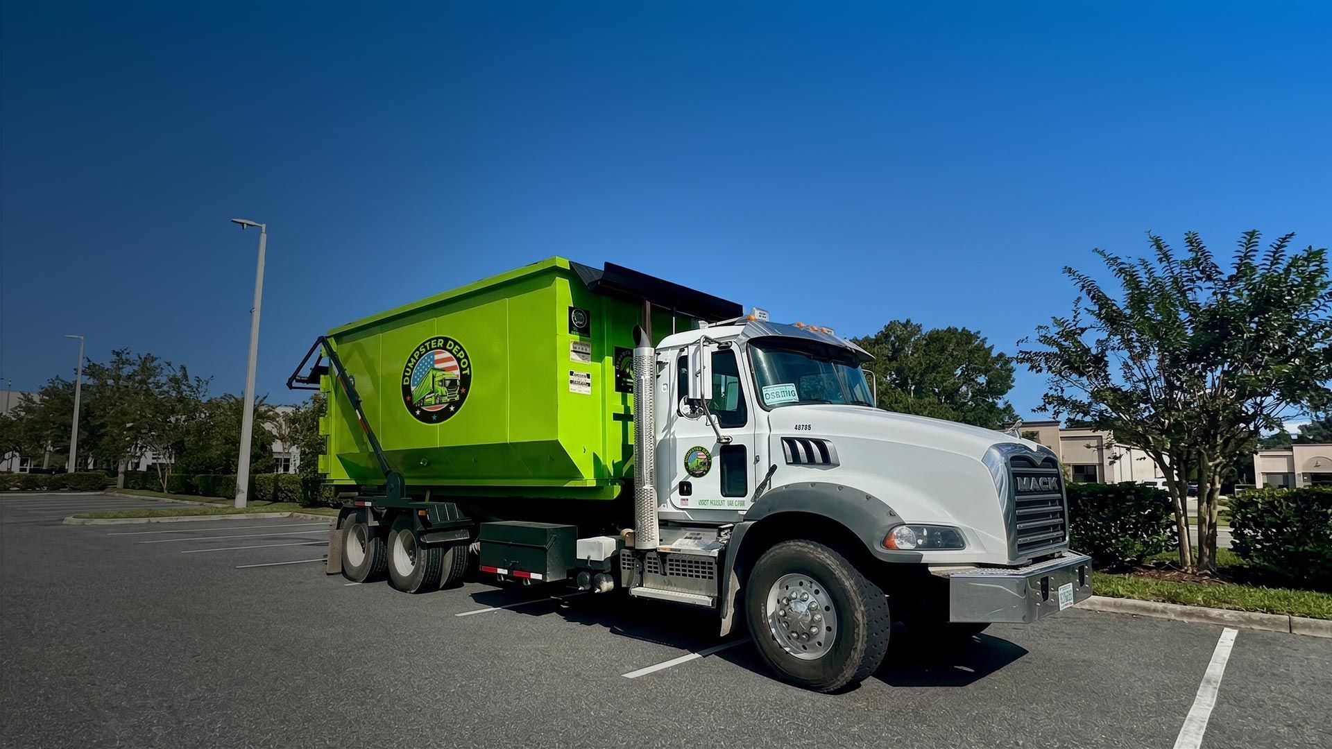 Green trash truck parked in a lot under a clear blue sky