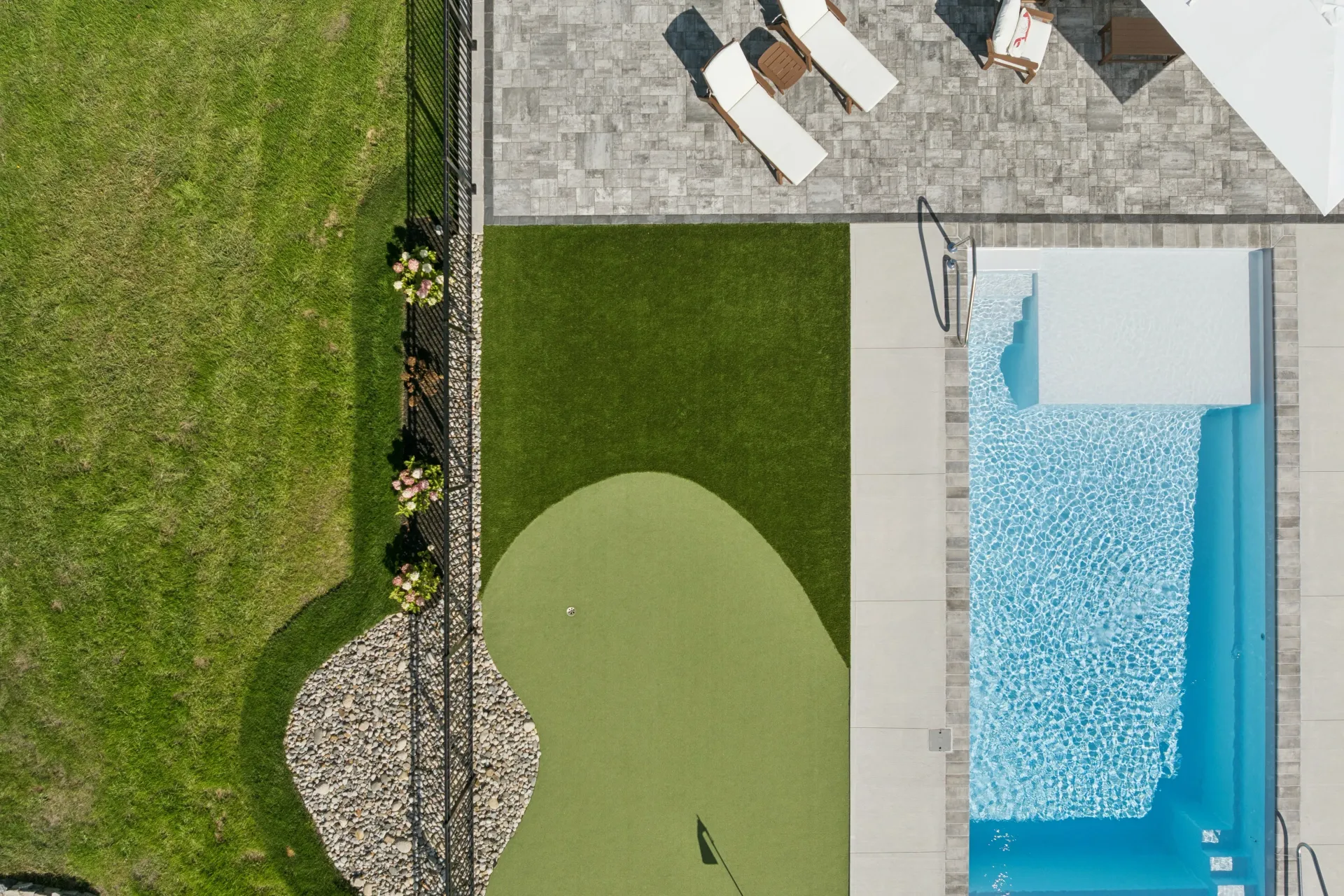Aerial view of a backyard with a pool, putting green, patio, and lawn.