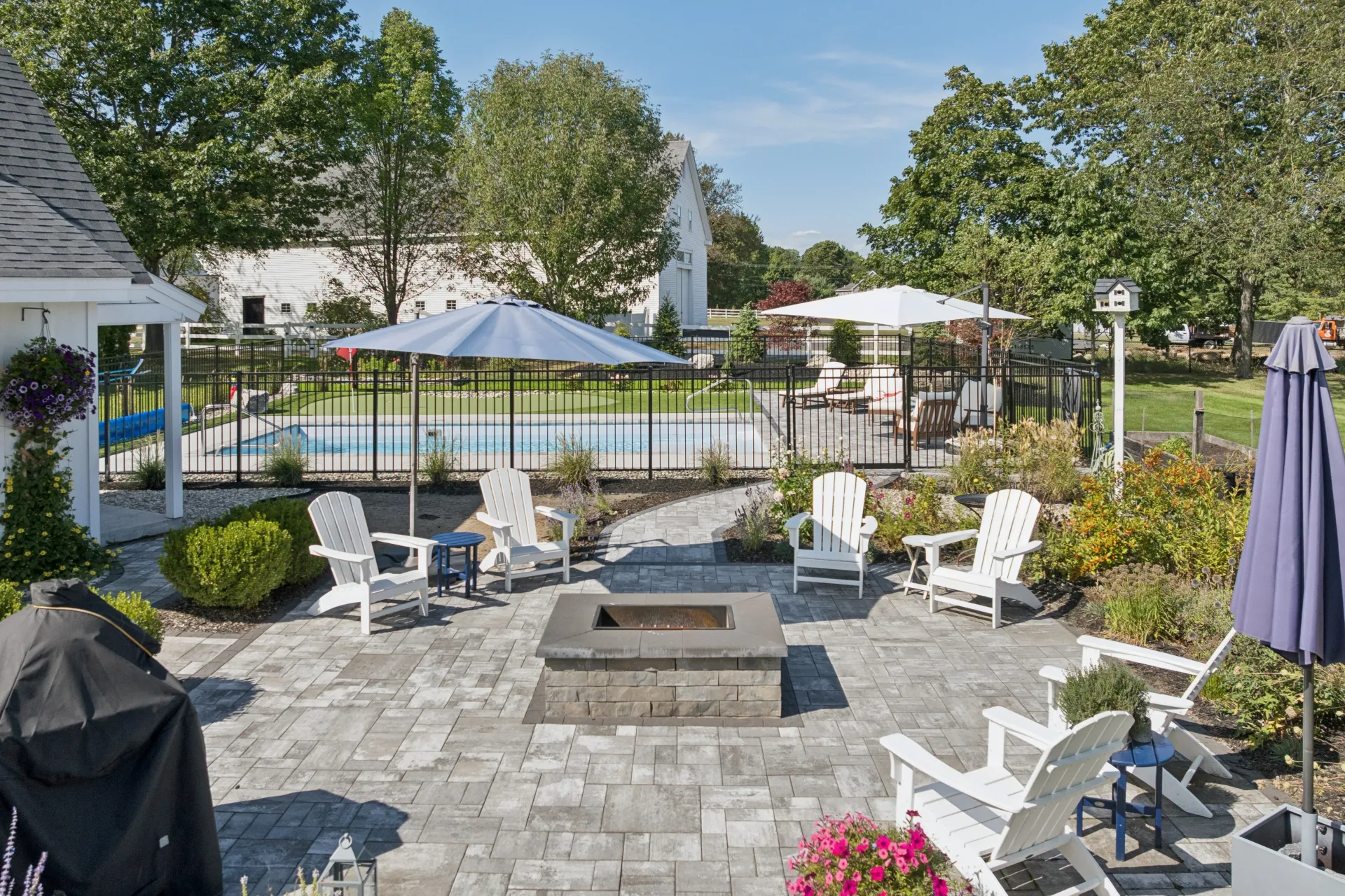 Patio with fire pit, Adirondack chairs, and pool in a backyard on a sunny day.