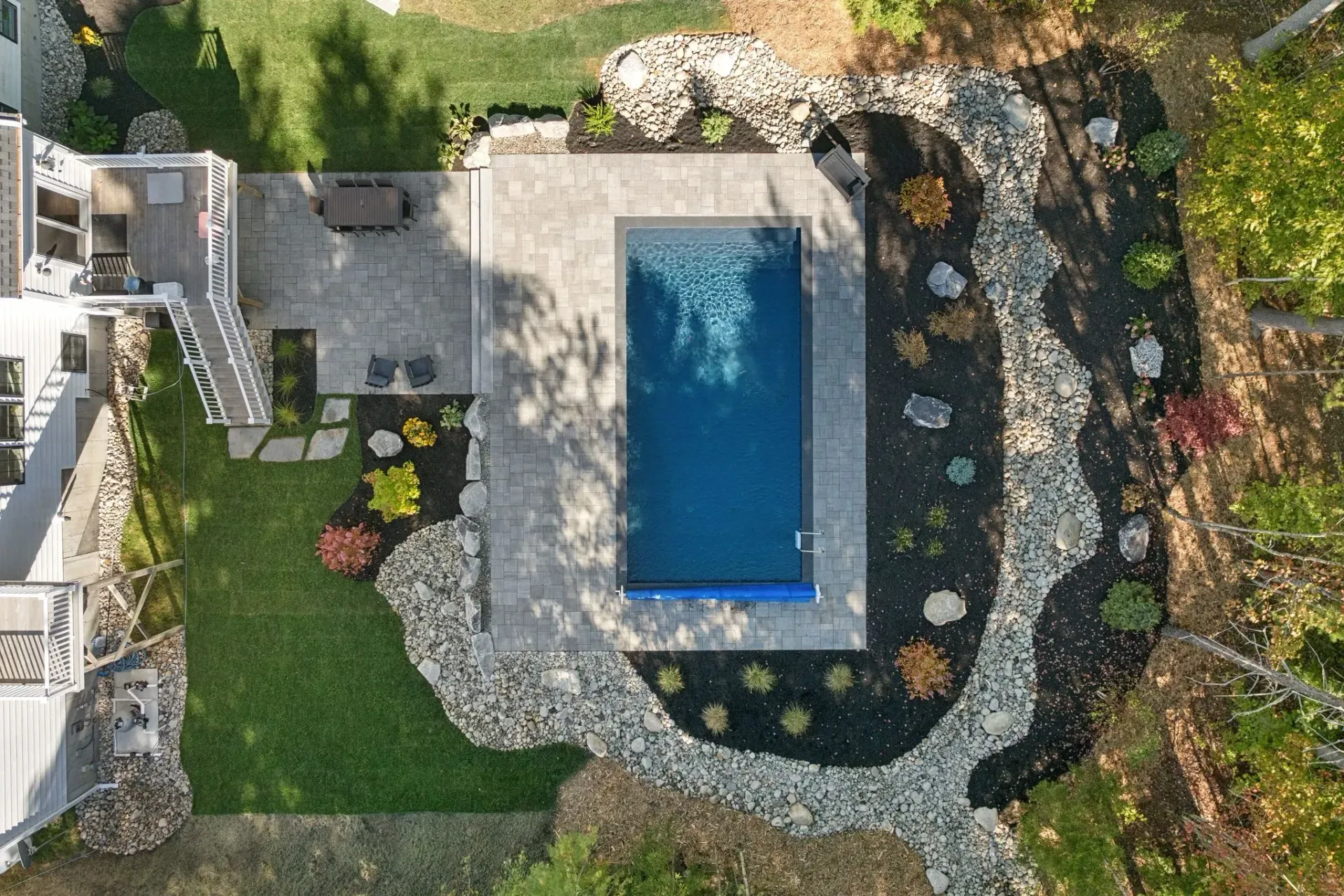 Overhead view of a rectangular pool surrounded by stone landscaping. Lawn and a deck are also visible.