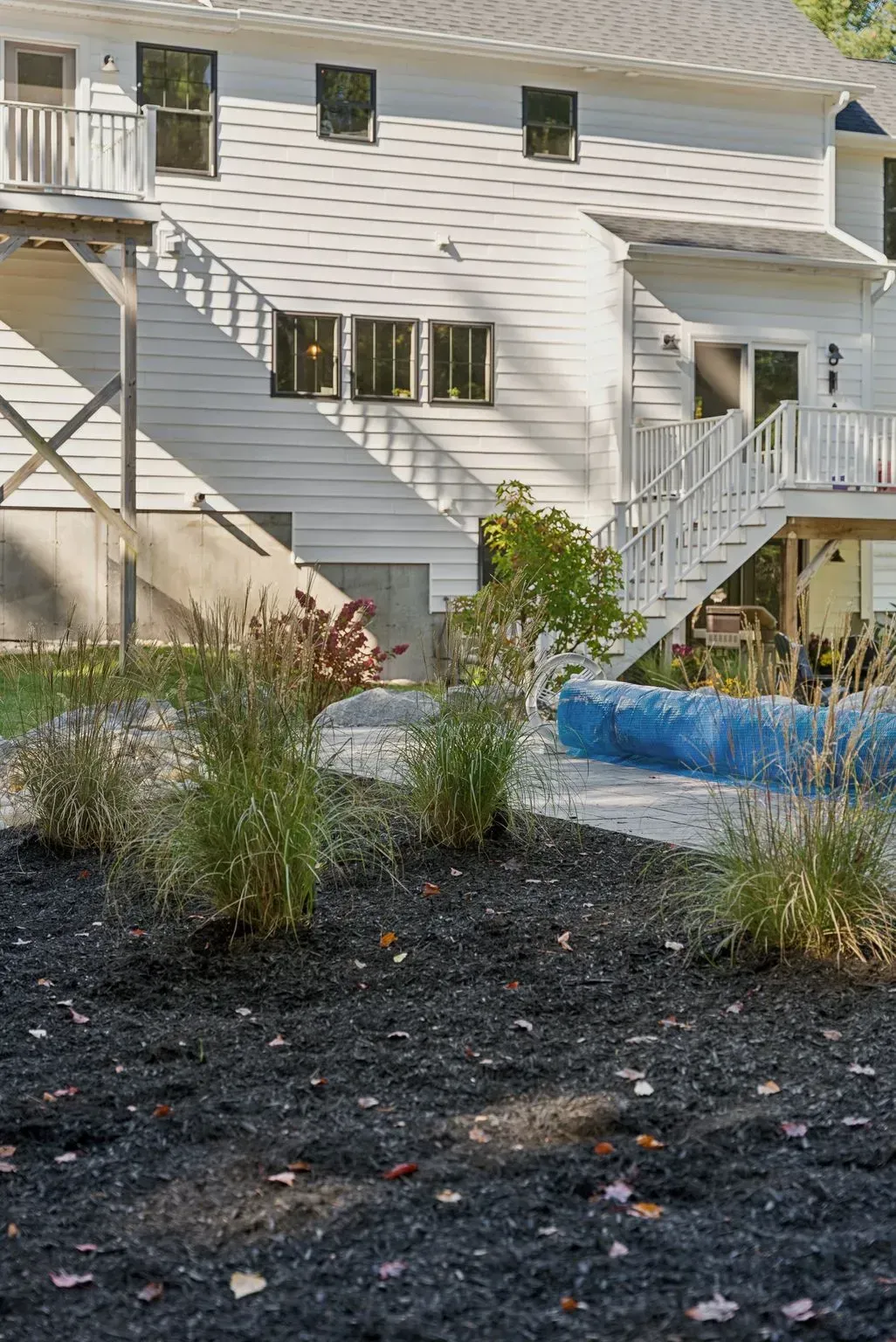 Back of a white building with exterior stairs and landscaping featuring dark mulch and plants.