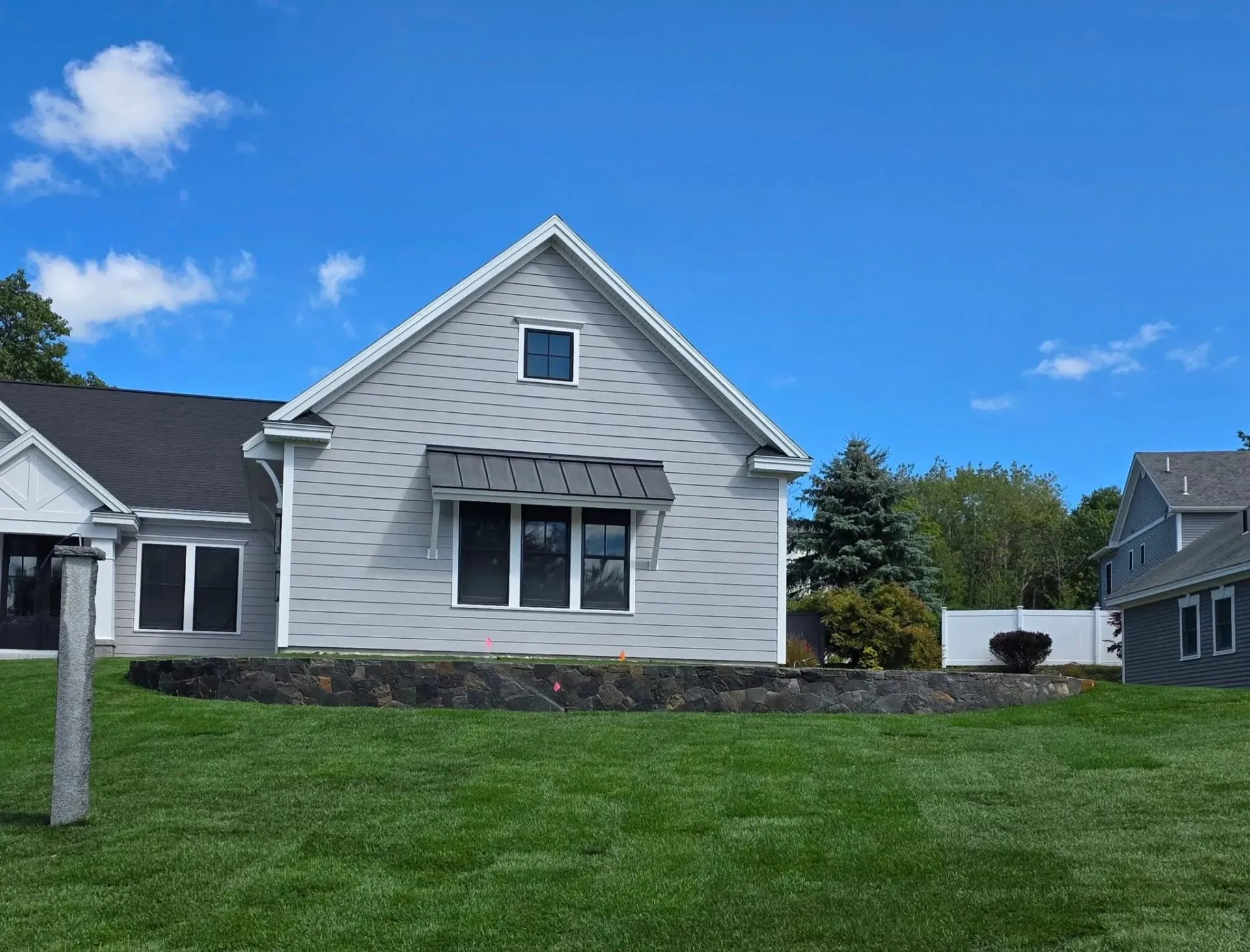 A light gray house with black awnings and a dark roof, on a green lawn against a blue sky.