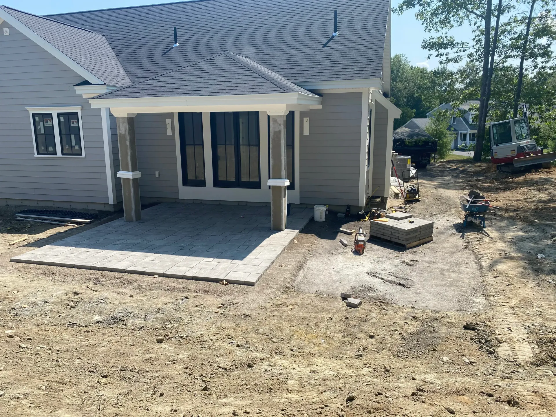 A house with a newly constructed patio; gray walls, black doors, and light gray pavers.