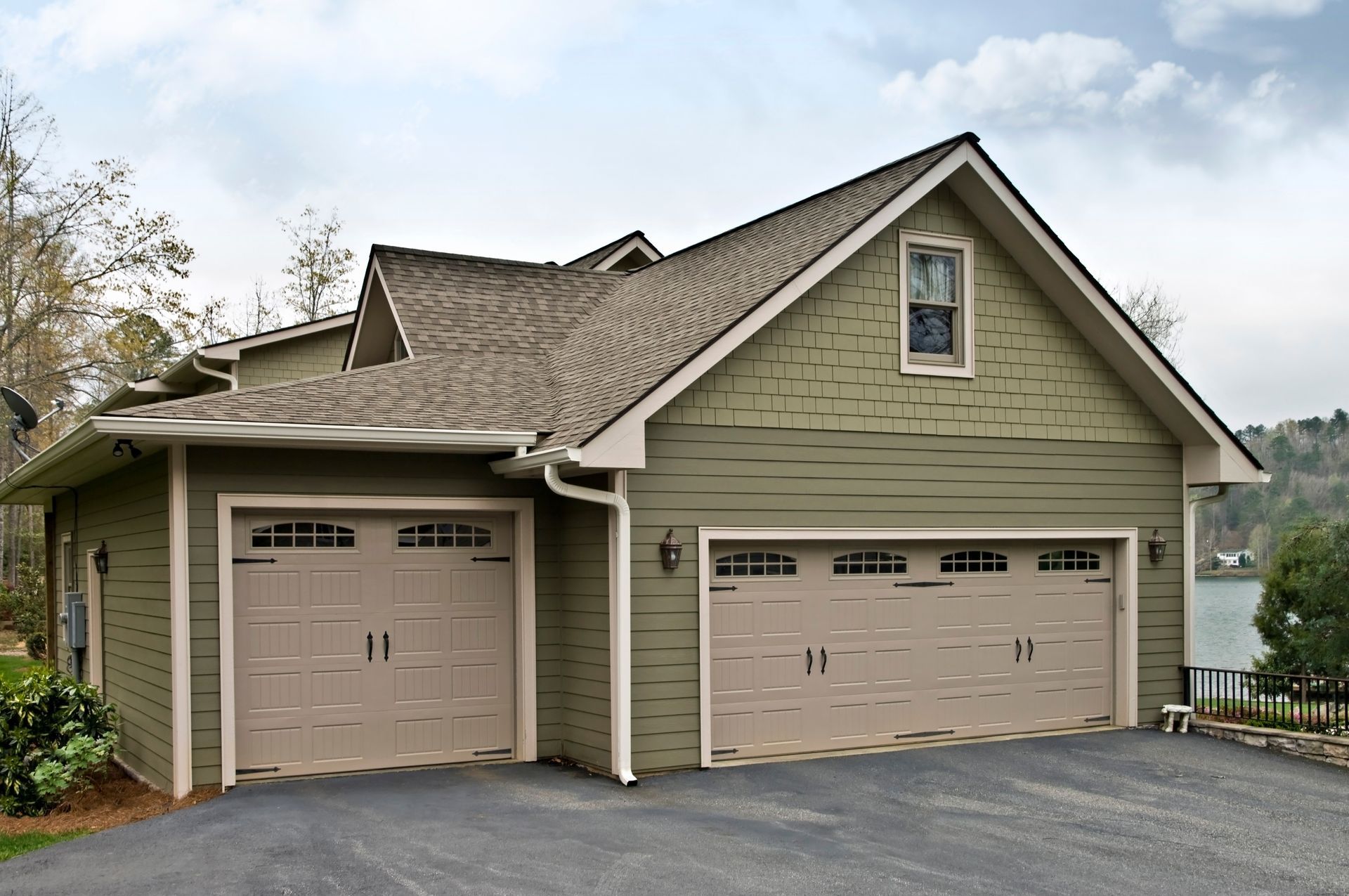 A green two-car garage with a single-car bay attached, featuring tan garage doors and a grey shingled roof.