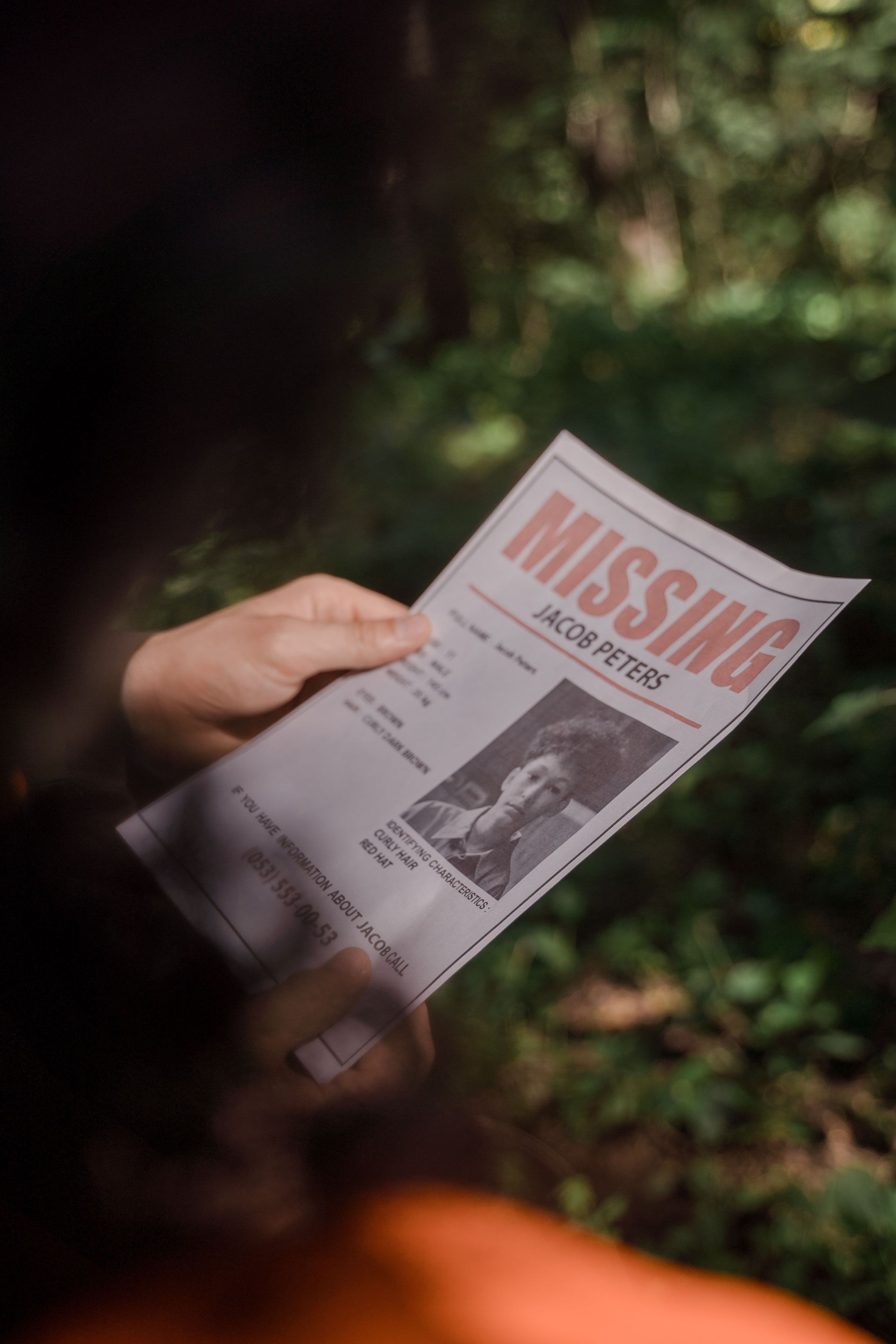 Hand holding a missing person flyer in a wooded area