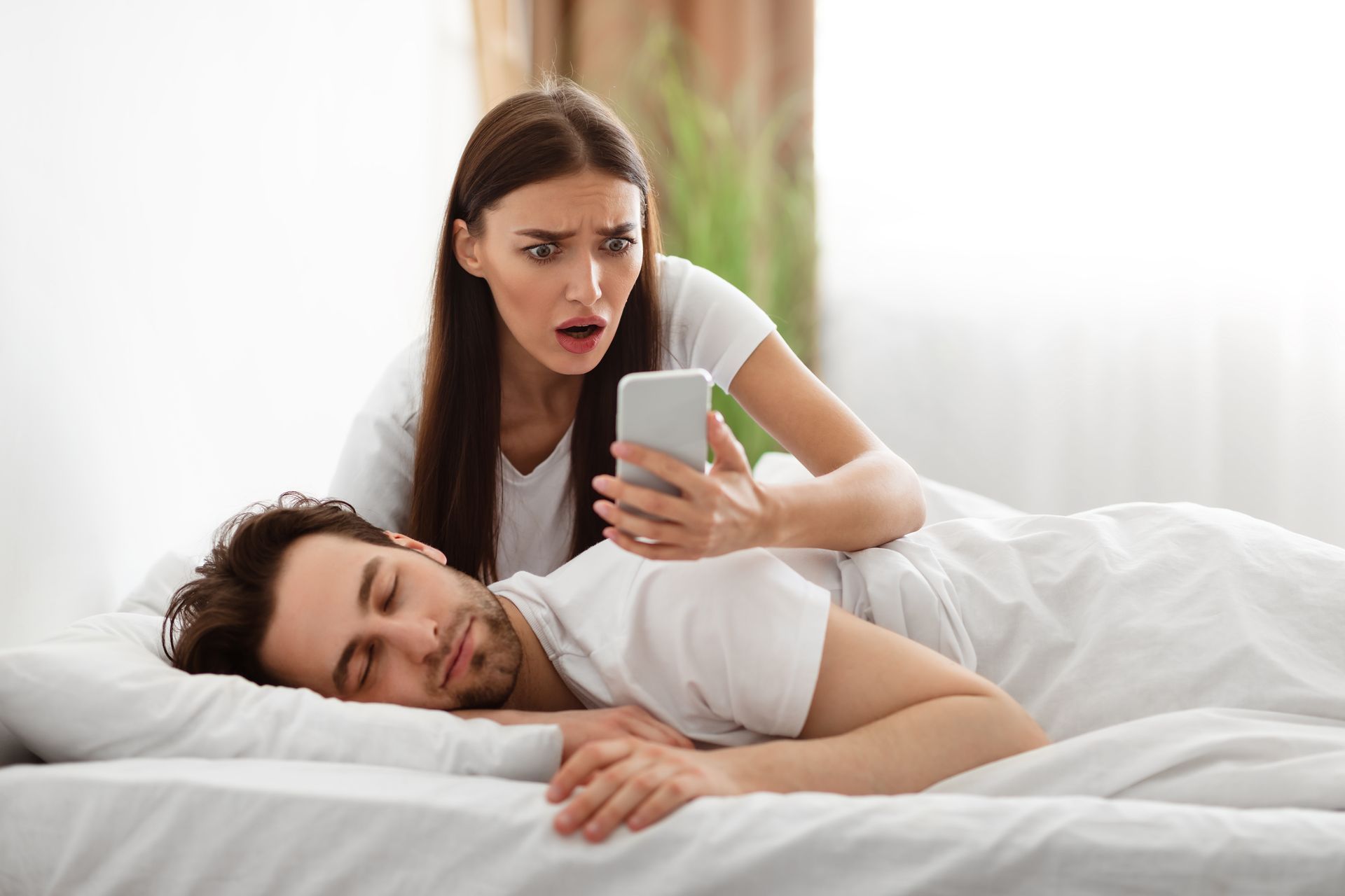 Concerned woman checking a sleeping partner's smartphone for infidelity investigation services in Cape Coral and Fort Myers.