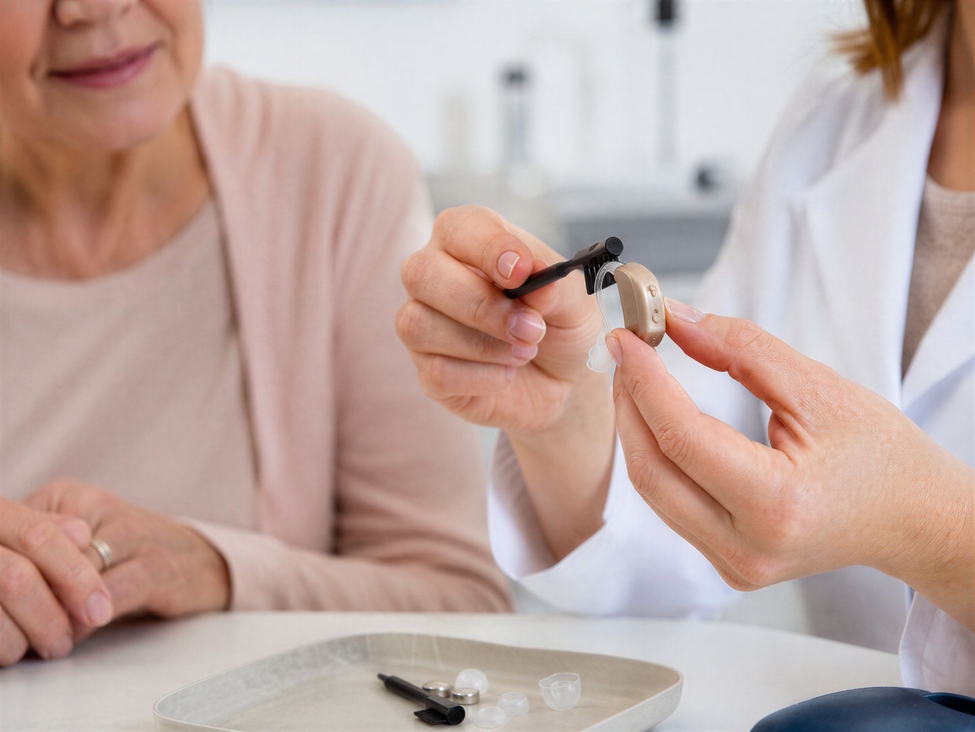 Audiologist adjusting a modern hearing aid for an elderly man in a medical clinic office.