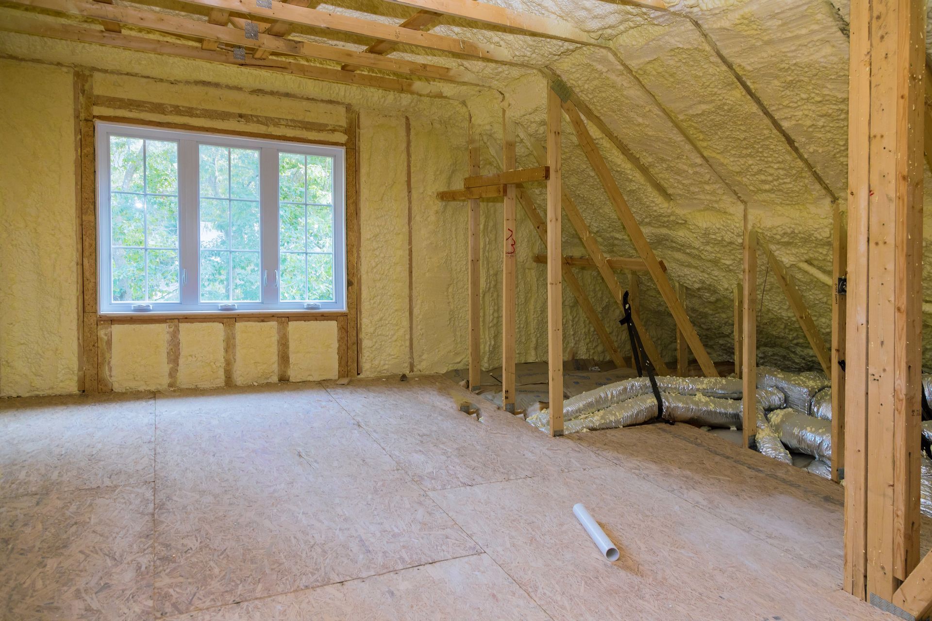 Insulated attic room under construction with exposed wooden framing and a window.