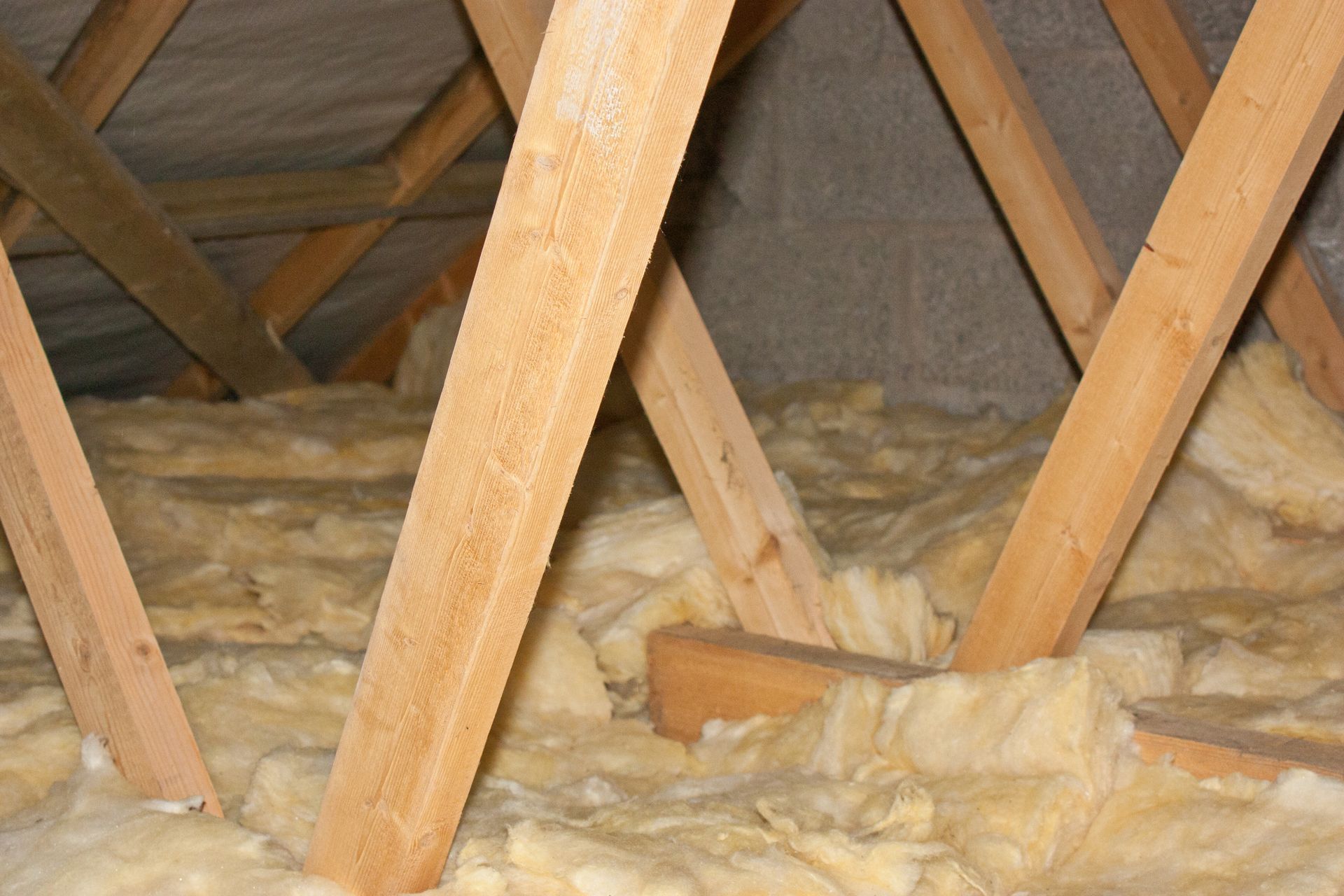Attic roof framing with wooden beams and yellow insulation batts between rafters