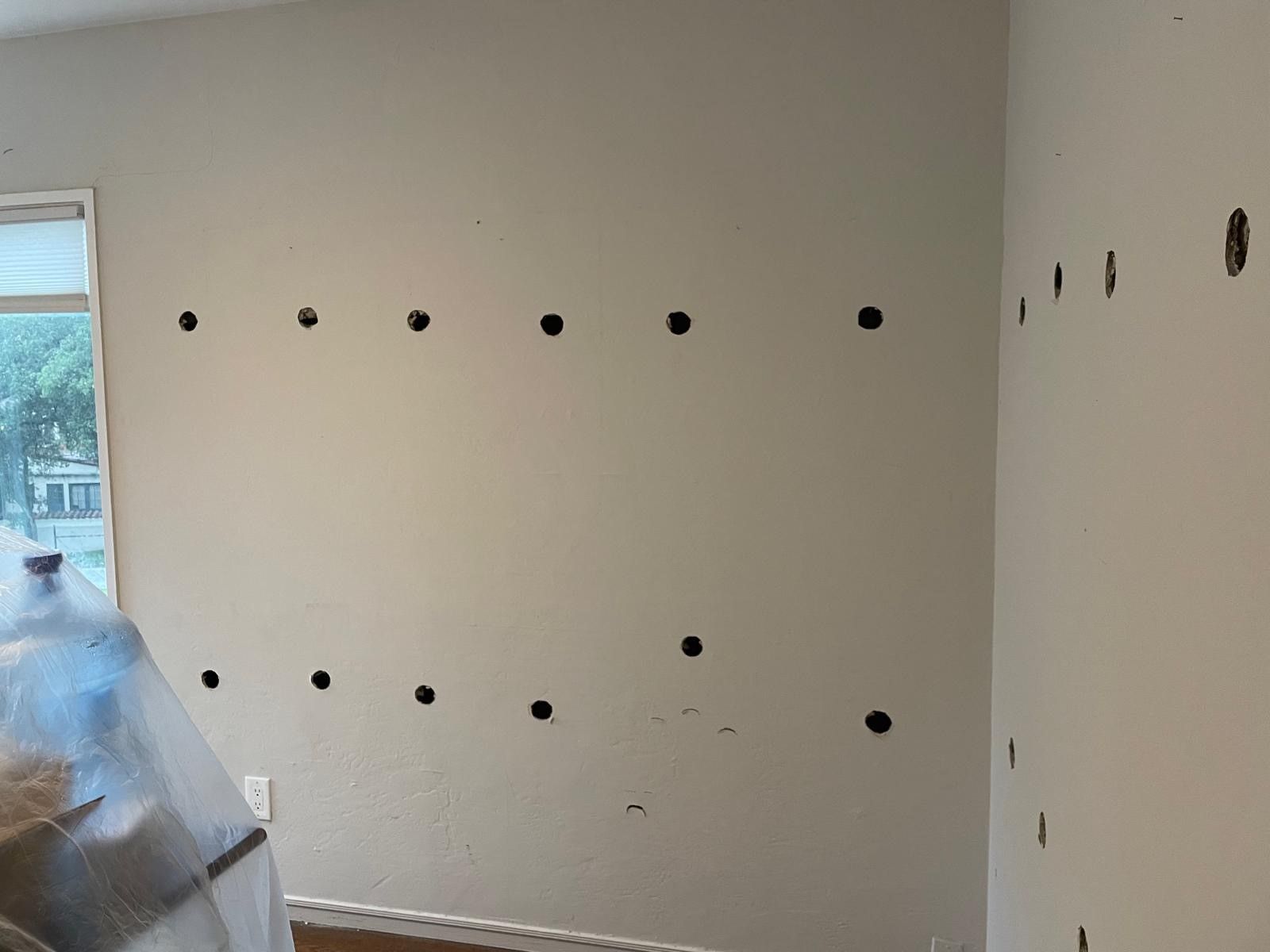 Empty room with rows of evenly spaced holes in beige walls, near a window on the left.