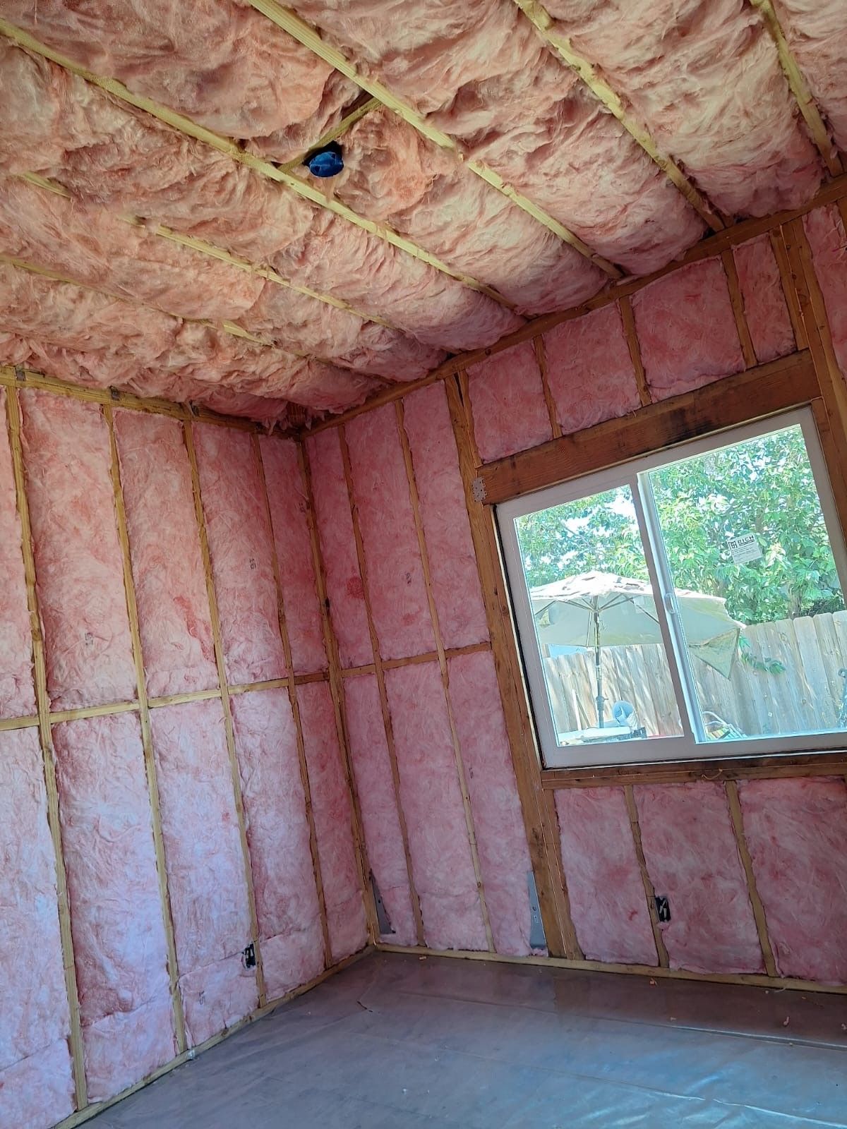 Insulated room under renovation with pink fiberglass walls, exposed ceiling, and a window on the right
