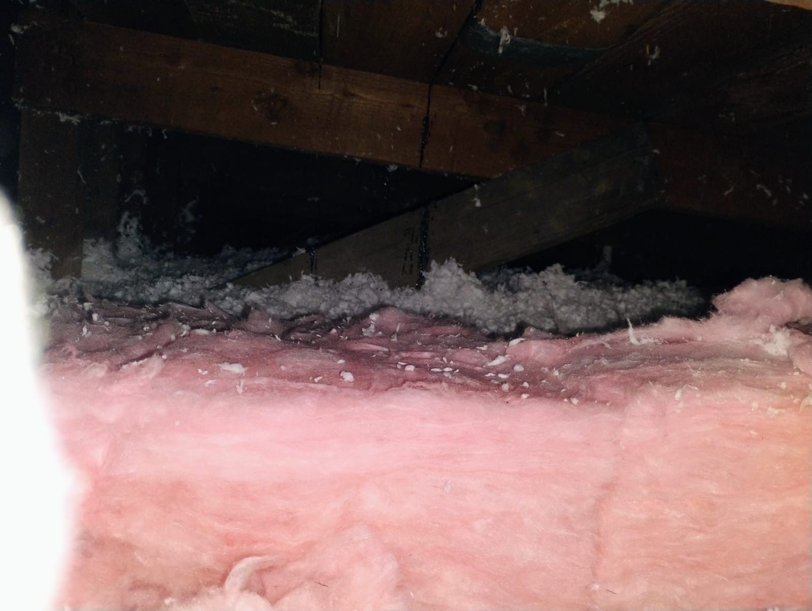 Pink insulation filling a dark attic space beneath wooden beams