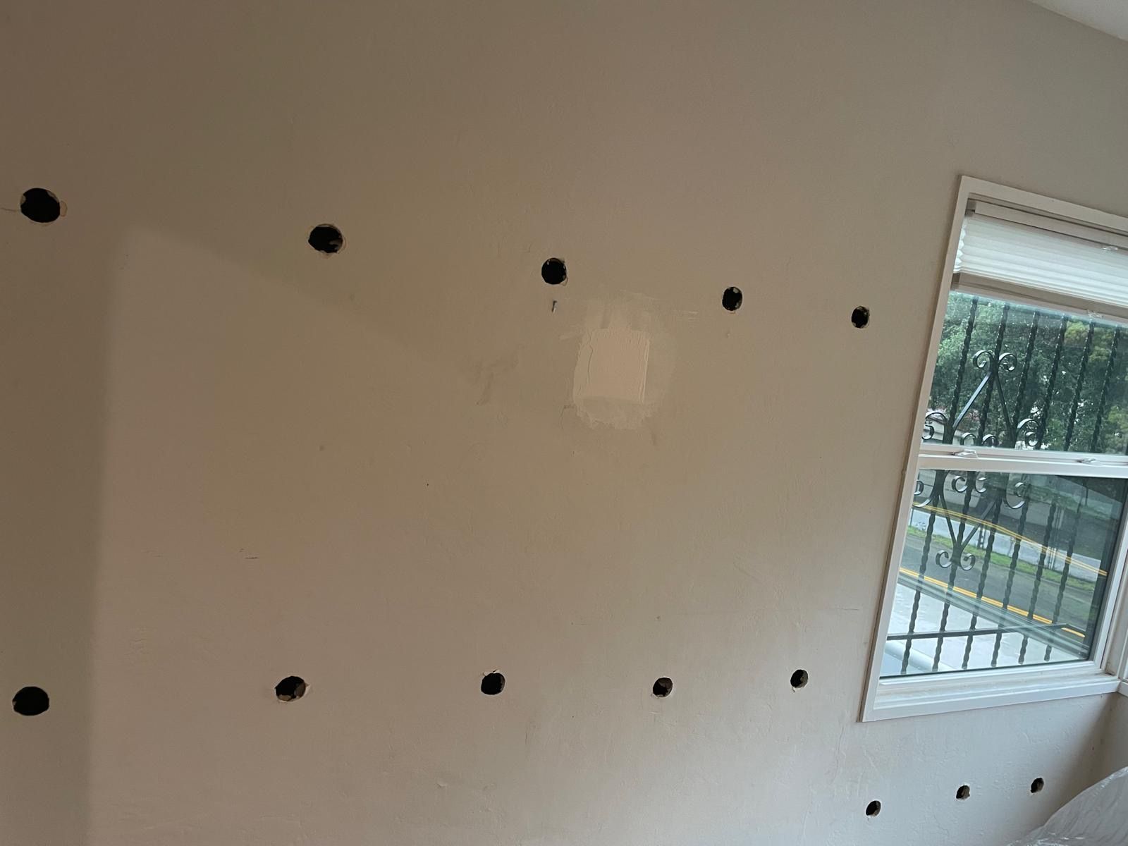 Wall with evenly spaced black holes beside a window and railing outside