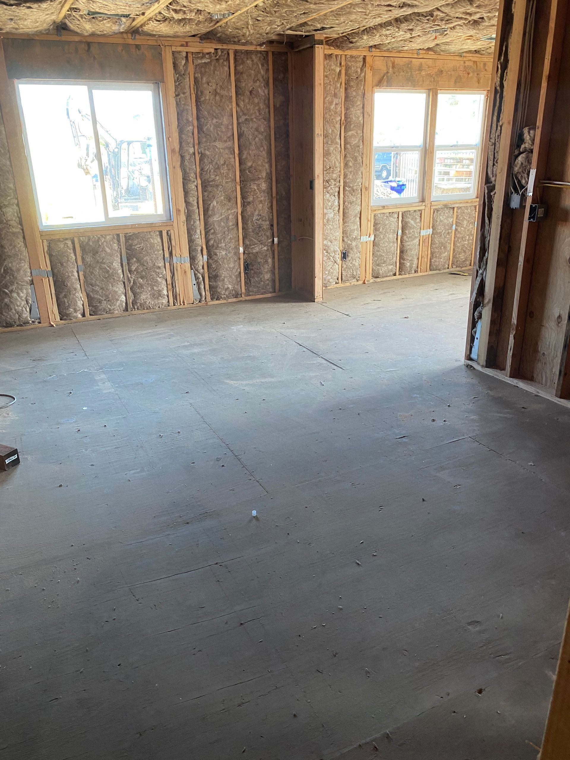 Unfinished room with exposed insulation, concrete floor, and two windows letting in daylight.