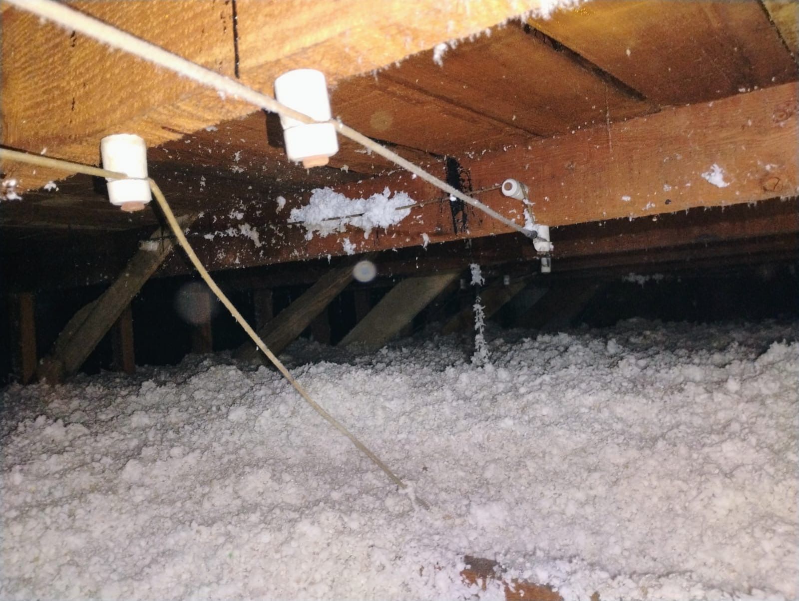 Attic with exposed wooden beams and insulation covered in piles of white blown-in material