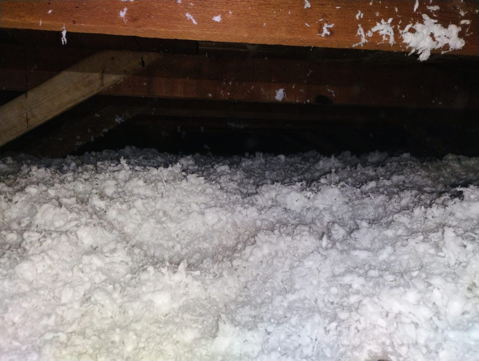 Snow piled under a wooden deck with a dark crawlspace above
