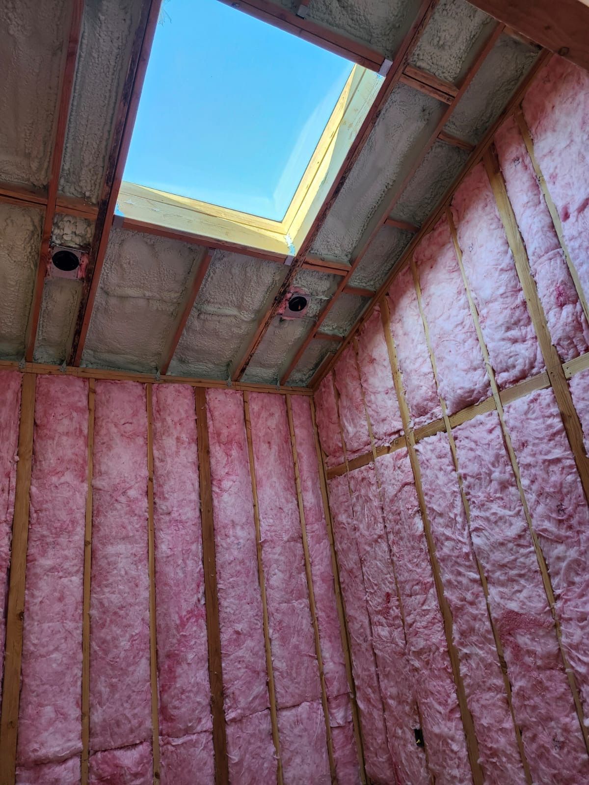 Insulated attic with pink foam walls and a skylight opening showing blue sky
