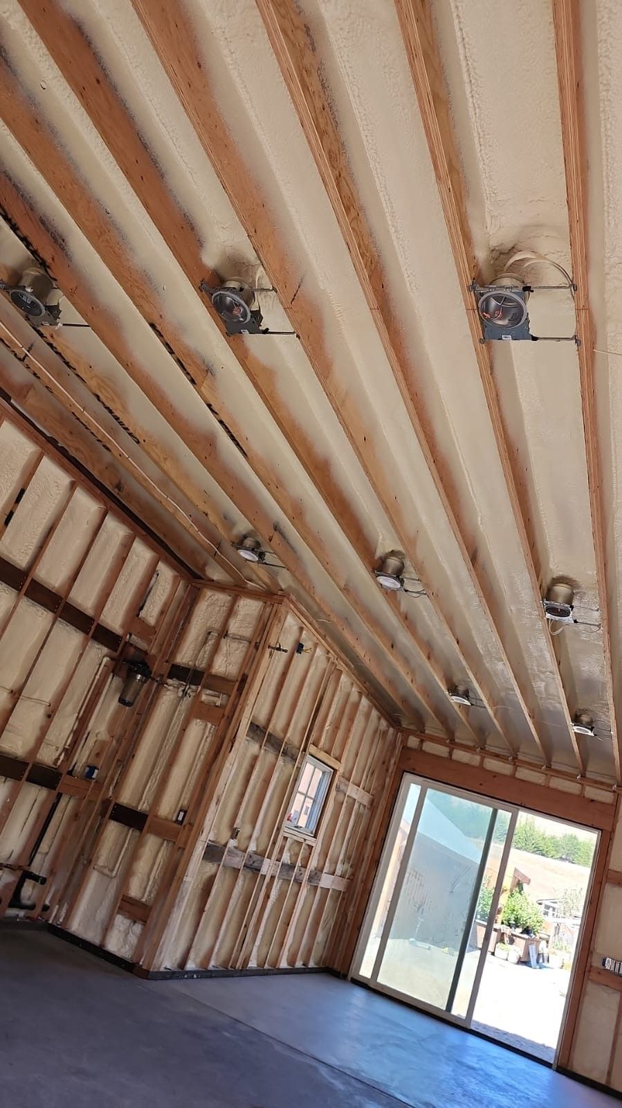 Unfinished room with exposed wall and ceiling framing, drywall stacks, and a sliding glass door opening outside