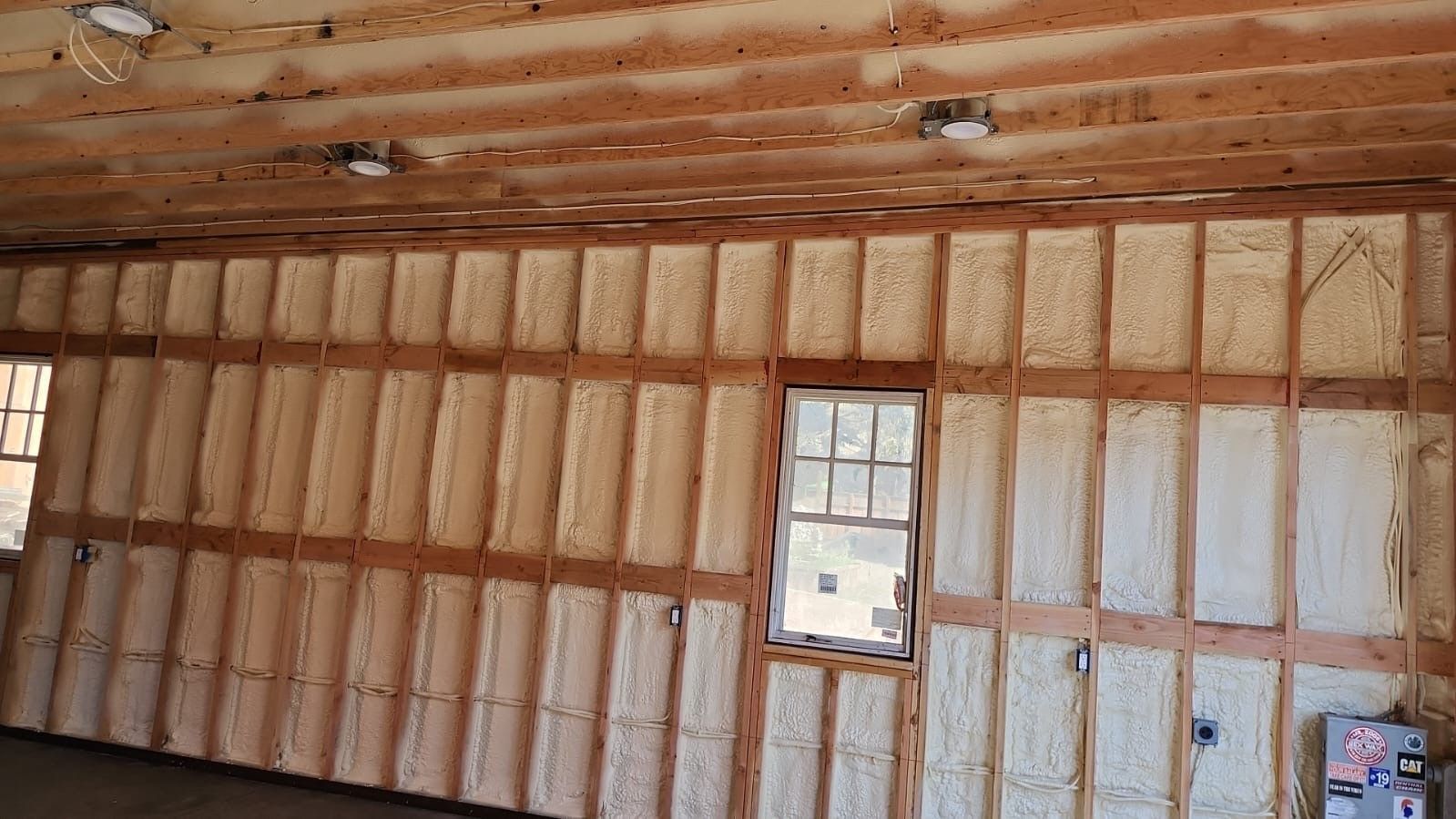 Insulated unfinished room with exposed wooden studs, ceiling joists, and a small window.
