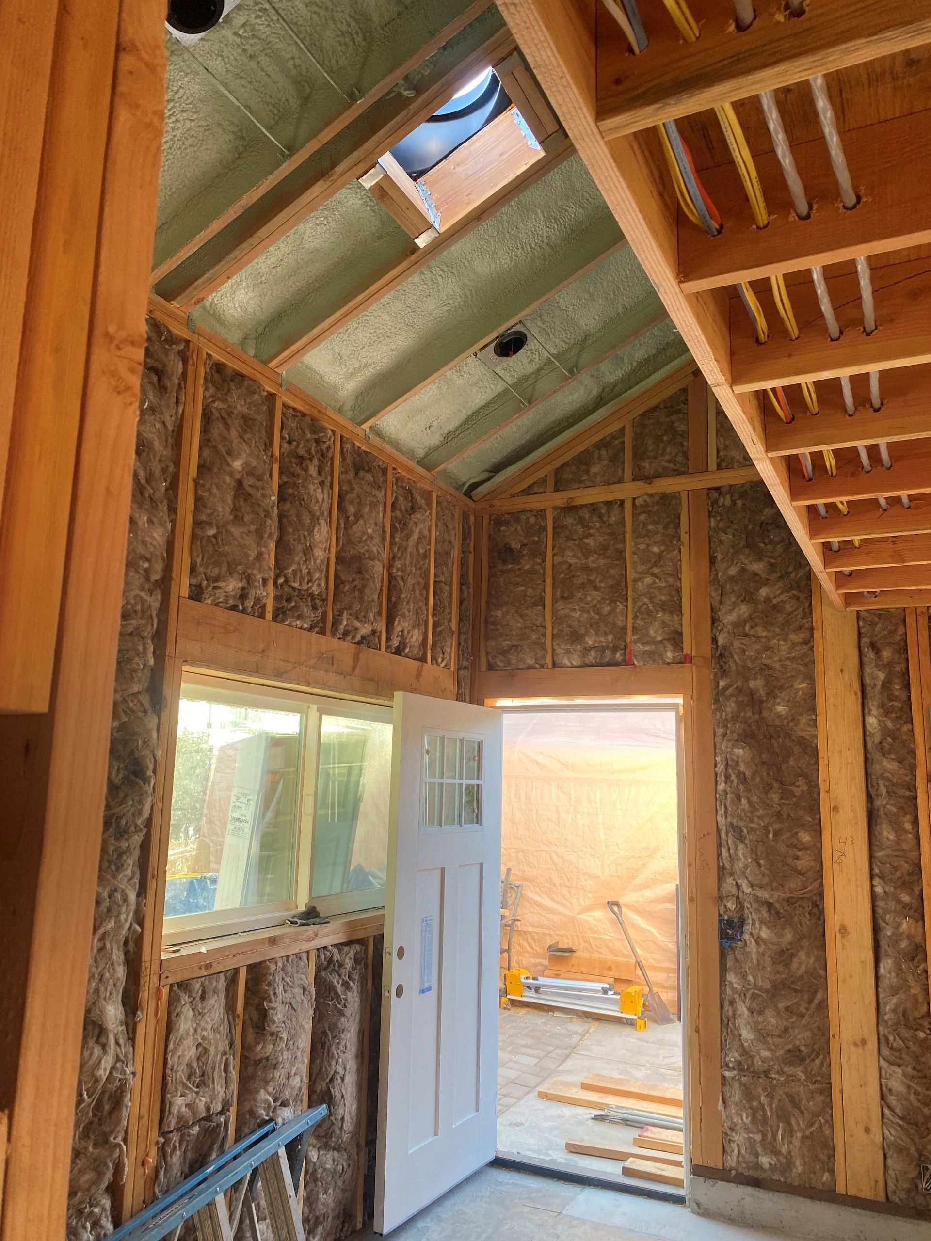 Exposed framing of a small room under construction with open doorway, window, and unfinished ceiling.