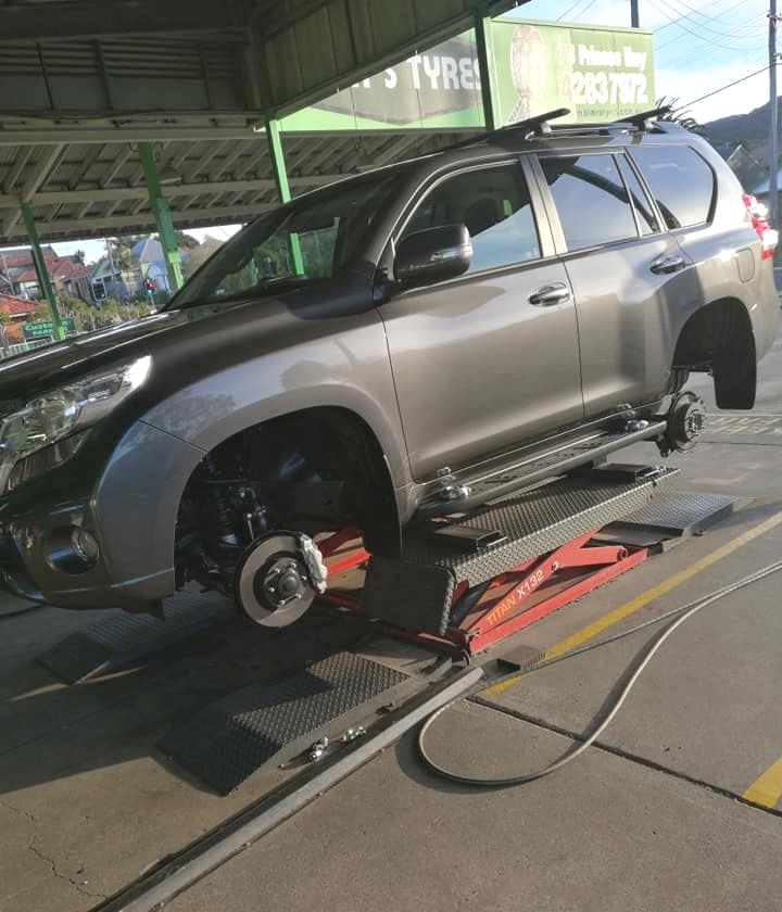 Grey SUV on a Lift at a Tire Shop, Front Wheels Removed, Sunny Day — D R Automotive in Russell Vale, NSW
