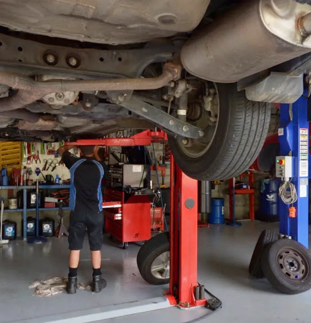 A Mechanic Working On a Car Lifted On A Hoist — D R Automotive in Russell Vale, NSW
