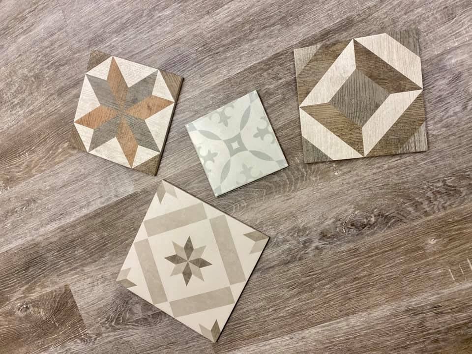 Four tiles with different designs are sitting on a wooden floor.