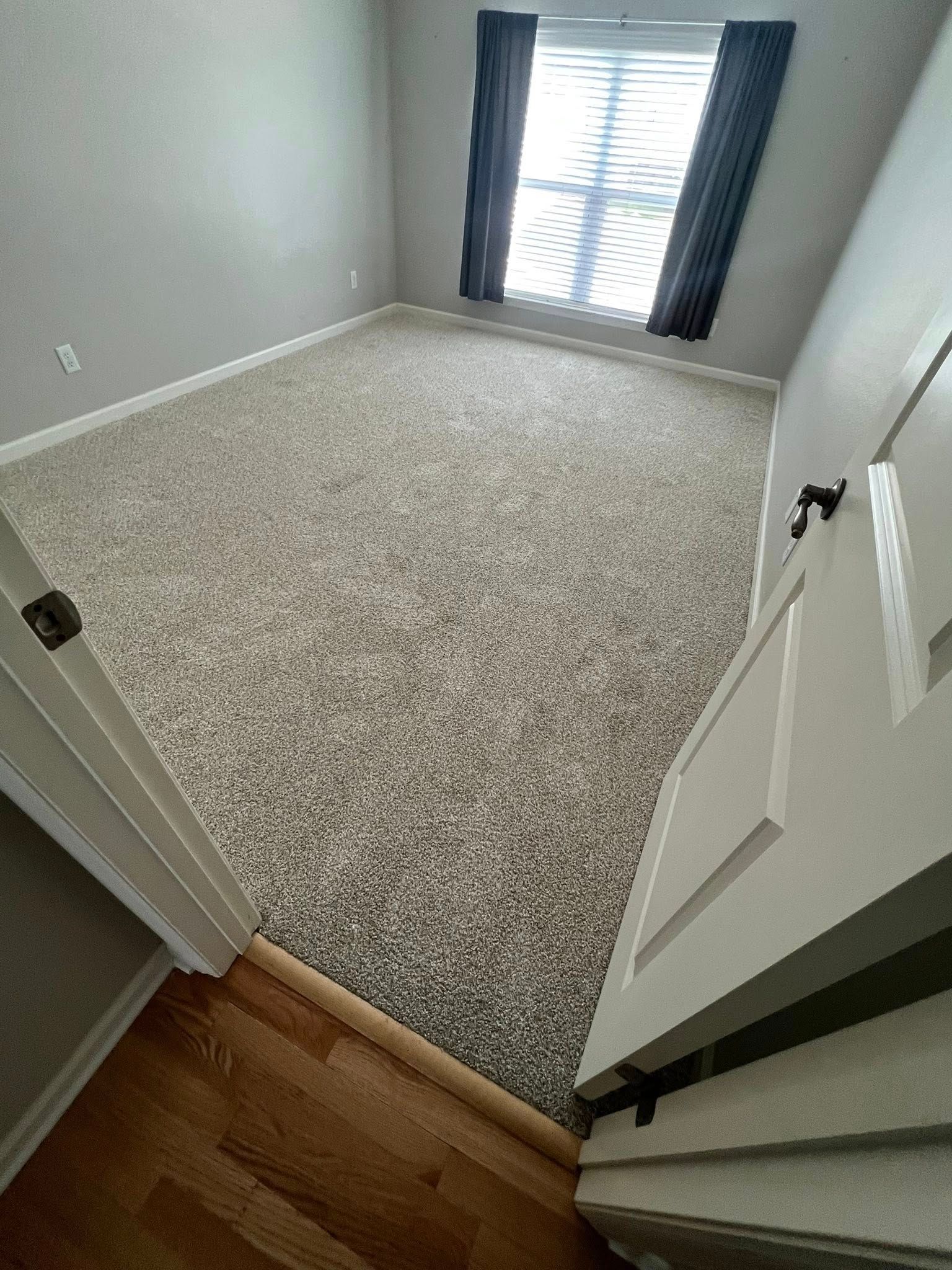 A bedroom with a large carpeted floor and a window.