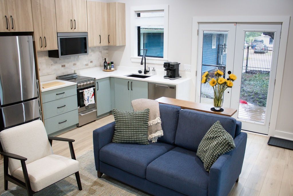 Small kitchen and living room, featuring blue sofa and light wooden cabinets.