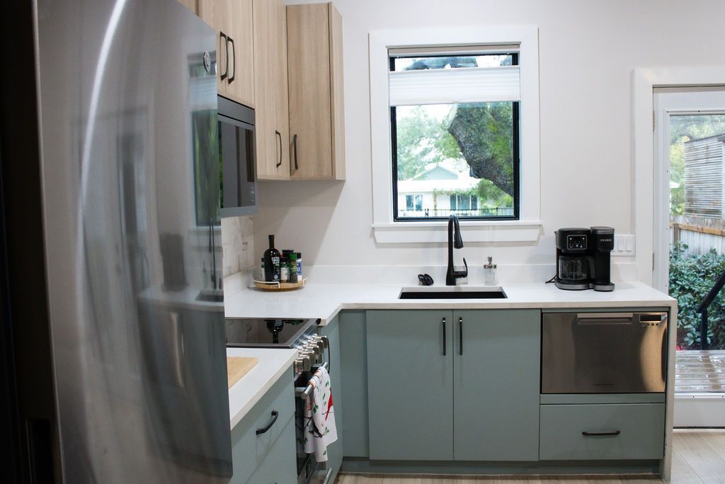 Modern kitchen with light blue and wood cabinets, stainless steel appliances, and a window.