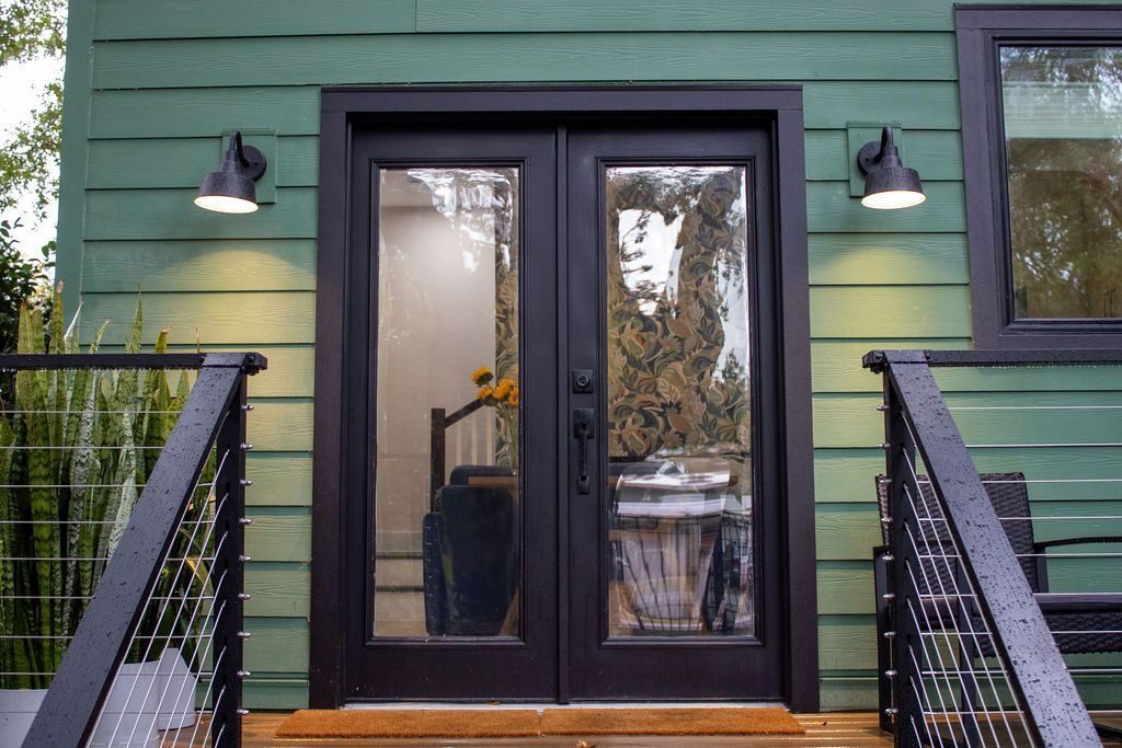 Green house with black double doors, two lights, and a deck.