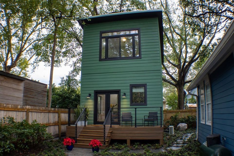A tall, green two-story house with a wooden deck and a black door and windows.
