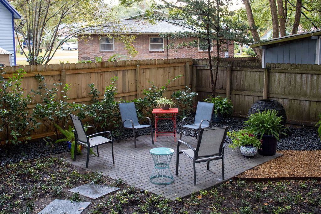 Patio with seating, surrounded by a wooden fence, plants, and small tables; a backyard scene.