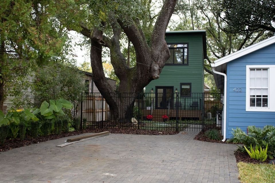 Green house behind a large tree, blue house to the right, and brick driveway.