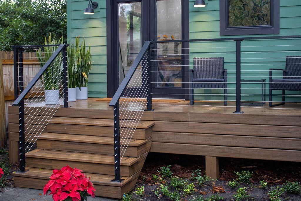 A green house with a wooden deck and stairs leading up to it.
