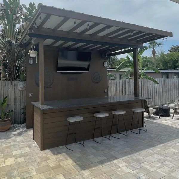 a patio with a bar, stools, a television and a pergola