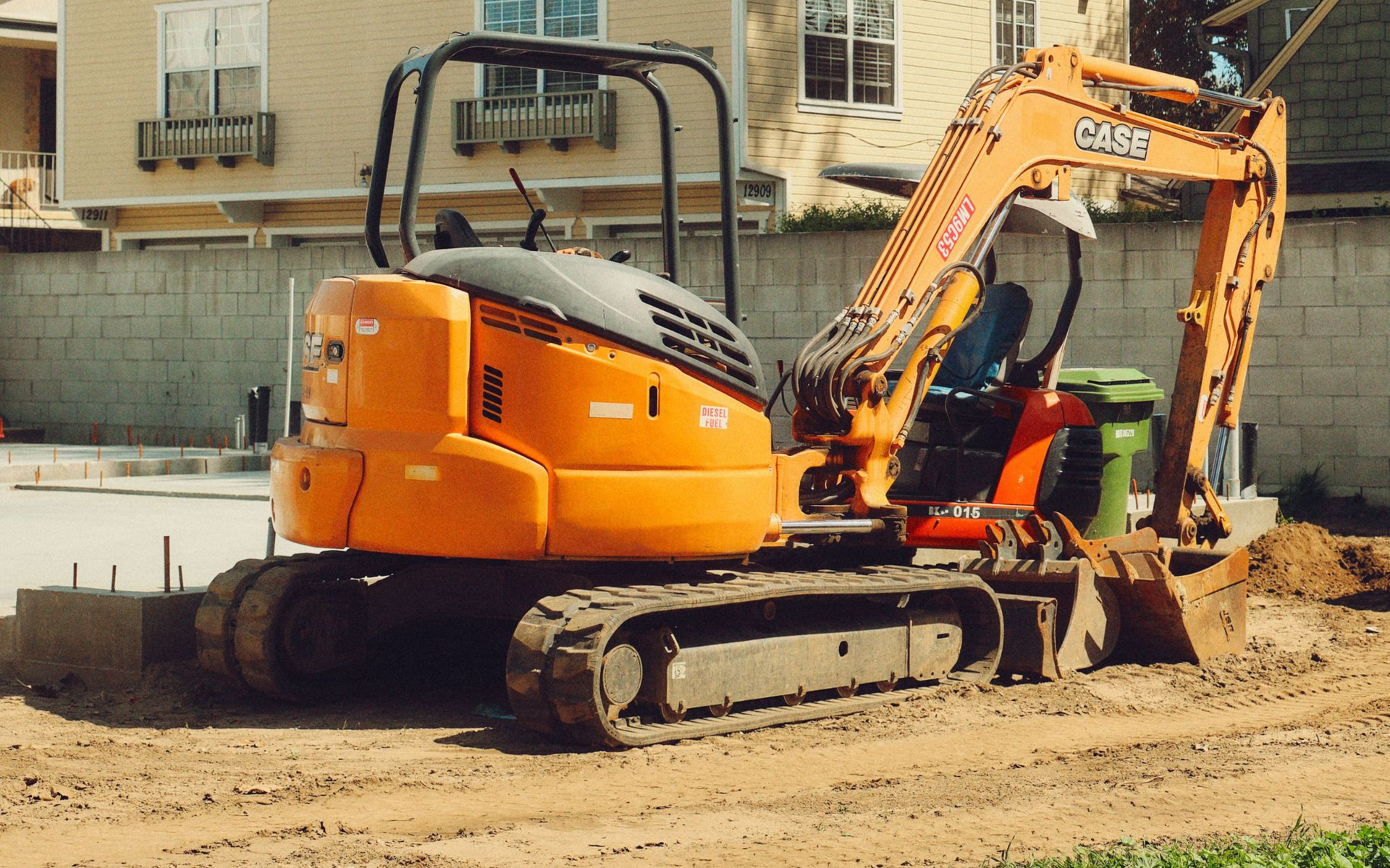 Orange excavator on tracks digging in a sandy construction site near a building.