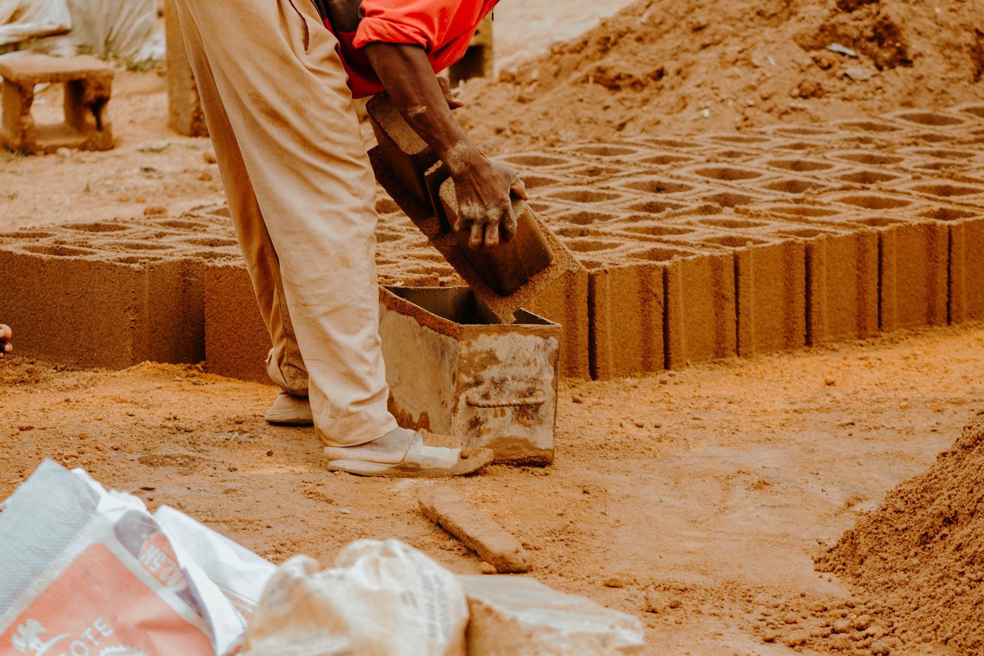 Worker laying wet clay bricks outdoors with a trowel