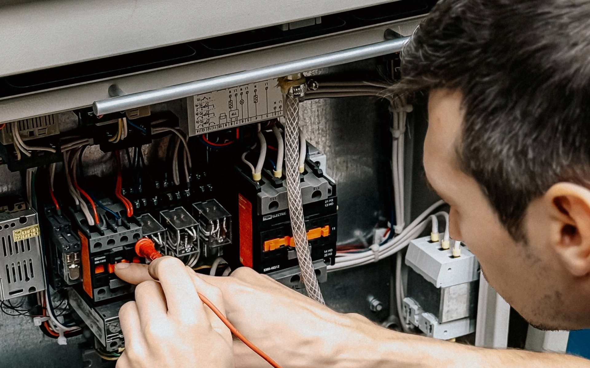 Technician using a multimeter to inspect wiring inside an electrical control panel