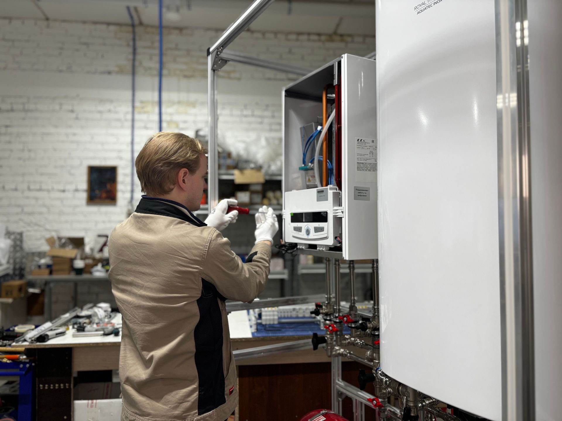 Person inspecting an open electrical control cabinet in a workshop, wearing gloves.
