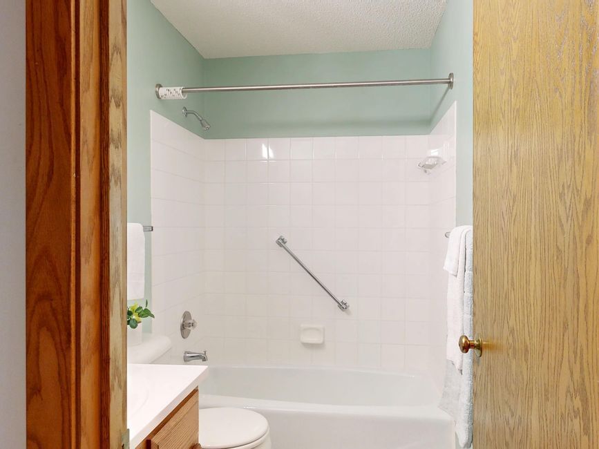 Small bathroom with white tub, shower rod, glass shelf, and wood door trim